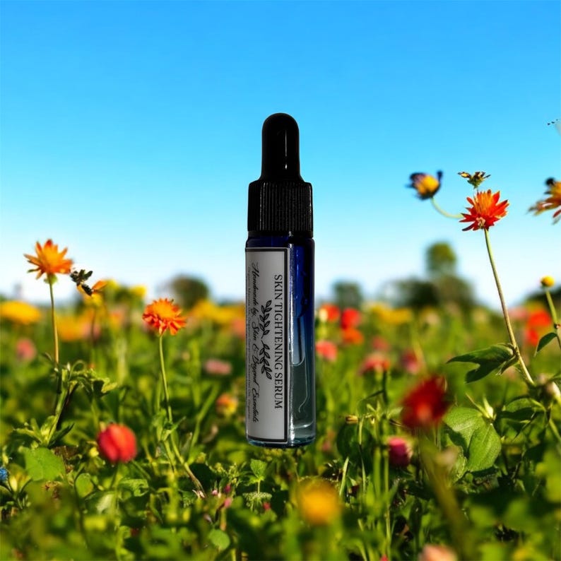 Pu&ograve; includere: Un piccolo flacone di vetro blu con un contagocce. Il flacone &egrave; etichettato "SKIN TIGHTENING SERUM" e "Handmade by Sea & Beyond Essentials". Il flacone &egrave; posto in un campo di fiori.