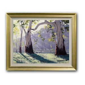 May include: A framed landscape painting featuring two large eucalyptus trees with white and dark brown trunks in the foreground. Sunlight filters through the branches, casting long shadows across a grassy field with a fence in the distance.