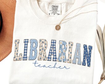 May include: Ivory-colored t-shirt with the word "LIBRARIAN" in patchwork letters, featuring blue gingham, floral, and polka dot patterns. The word "teacher" is written in a cursive font below. A gold necklace and a hat are also visible.