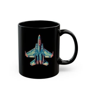 May include: Black ceramic coffee mug featuring a detailed illustration of a fighter jet in shades of blue, orange, and teal. The jet is centered on the mug, with the handle on the right side. A unique gift for aviation enthusiasts.