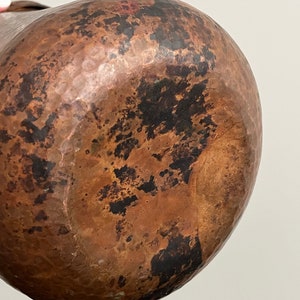 May include: A large, hammered copper pitcher with a brown patina. The pitcher has a rounded body and a wide mouth.