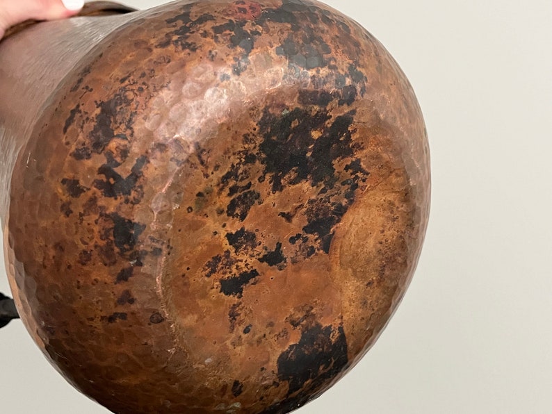 May include: A large, hammered copper pitcher with a brown patina. The pitcher has a rounded body and a wide mouth.