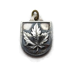 Op de afbeelding: Zilveren hanger in de vorm van een schild met een gestileerd esdoornbladontwerp.