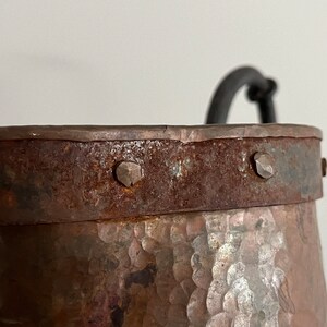 May include: A rustic copper bucket with a hammered finish and a black metal handle. The bucket has a metal band around the top with decorative rivets.