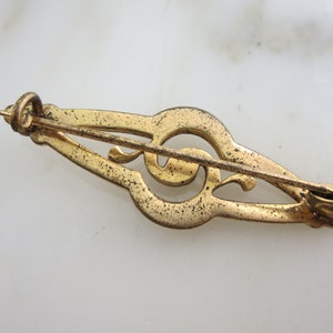 Pode incluir: Broche de clave de sol dourada com um design decorativo. A broche tem um fecho de pino e fecho.
