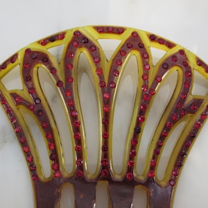 May include: A yellow and brown plastic hair comb with a decorative design and red rhinestones.