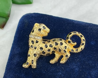 May include: A gold-tone brooch in the shape of a leopard with black enamel spots. The brooch has a row of clear rhinestones around the neck.