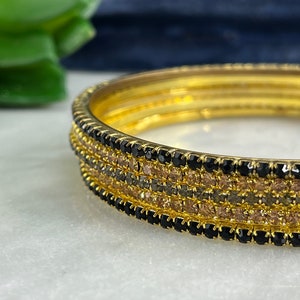 May include: Set of four gold bangles with black and brown crystal embellishments.
