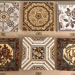 Może przedstawiać: Sześć zabytkowych płytek ceramicznych z misternymi wzorami kwiatowymi i geometrycznymi w odcieniach brązu, żółtego i białego. Płytki są ułożone w dwóch rzędach po trzy, każda płytka ma unikalny wzór.