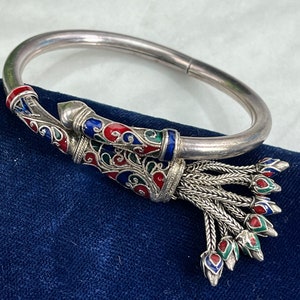May include: A silver bangle bracelet with a colorful enamel design and a tassel. The enamel is red, blue, and green. The tassel is made of silver chains.