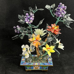 May include: A jade and gemstone flower arrangement in a blue and gold cloisonné pot. The flowers are made of various colored gemstones, including amethyst, jade, and orange.