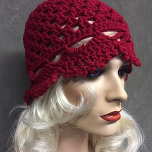 May include: A red crocheted cloche hat with a scalloped edge. The hat is made with a lacy stitch pattern.