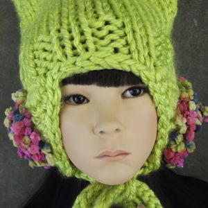 May include: A lime green knitted hat with ear flaps and a pom-pom detail. The hat is made with a chunky yarn and has a loose, slouchy fit.
