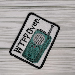 May include: White embroidered patch with black stitching. The patch features a green walkie talkie with the text "WTF2 Over!" in black.