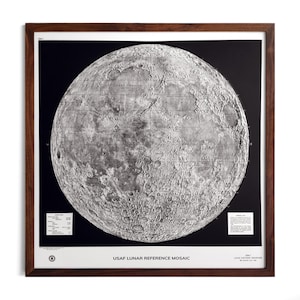 Puede incluir: Una impresión en blanco y negro enmarcada de la superficie lunar, con detalles de cráteres y marcas geográficas. La impresión se titula "USAF LUNAR REFERENCE MOSAIC" y está enmarcada en un marco de madera marrón oscuro, ideal para decoración.