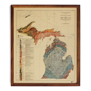 May include: A vintage geological map of Michigan, framed in a dark wood frame. The map is in relief, showing the different geological formations of the state. The map is titled "Geological Map of Michigan" and is dated 1908.