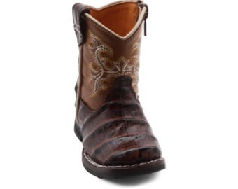 Peut inclure: Une botte de style western marron avec un pied marron foncé à motif texturé façon crocodile et une tige marron plus clair ornée de surpiqûres décoratives crème. La botte comprend une fermeture éclair latérale et une semelle marron foncé.