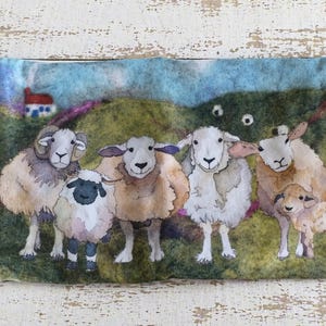 May include: A rectangular, fabric pouch featuring a watercolor painting of sheep in a green field with a small house. The pouch has a purple border and a cream-colored handle. A tag with the text "Emma Ballo" is attached.