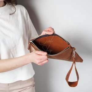 May include: A brown leather clutch with a zipper closure and a wrist strap. The clutch is open and the inside is lined with brown fabric.
