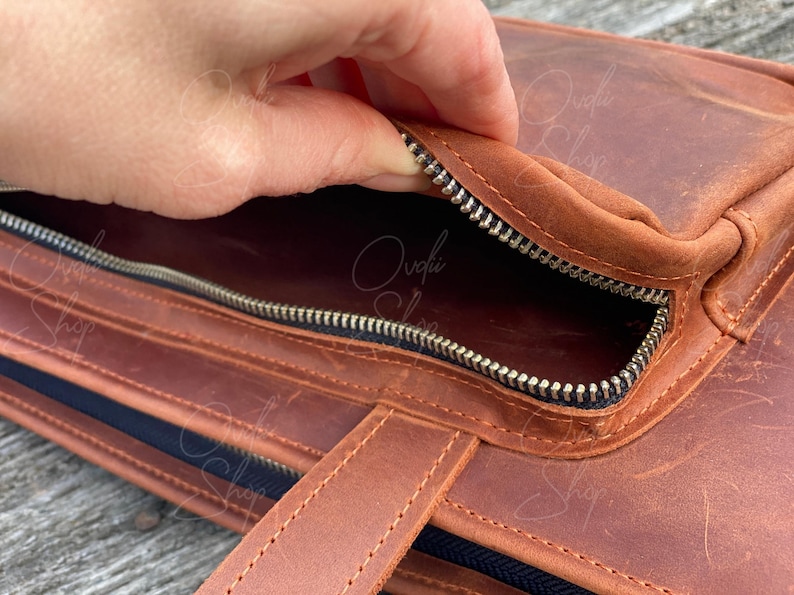 May include: A brown leather bag with a zippered pocket and a handle. The zipper is open and the inside of the bag is visible.