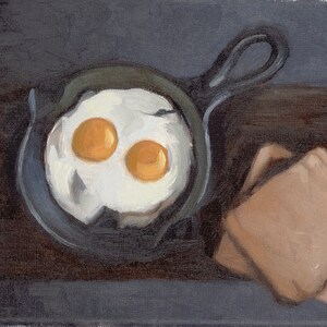 May include: A close-up of a cast iron skillet with two fried eggs and two pieces of toast on a dark brown surface.