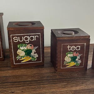 May include: Set of four wooden canisters with painted floral designs and labels for flour, sugar, tea, and coffee.