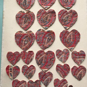 May include: A collection of heart-shaped fabric patches with a paisley design in red, blue, and white. The patches vary in size and are arranged on a white background, suggesting a craft project or decorative element.
