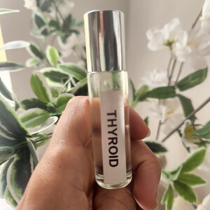 Op de afbeelding: Een transparante glazen rollerfles met een zilveren dop en een wit etiket met de tekst "THYROID".