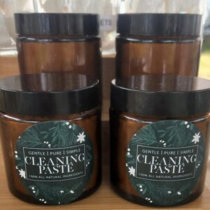 May include: Four amber glass jars with black lids and green and white labels that read "Gentle | Pure | Simple Cleaning Paste 100% All Natural Ingredients".