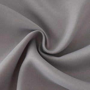 Può includere: Primo piano di un tessuto grigio chiaro con pieghe morbide e una trama sottile. Il tessuto sembra essere un materiale liscio e tessuto, possibilmente utilizzato per abbigliamento o arredamento per la casa. L'immagine evidenzia la drappeggiatura e il colore del tessuto.