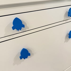 May include: Four blue rocket-shaped drawer pulls on a white dresser.