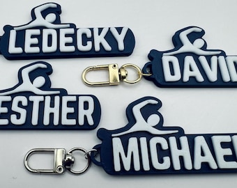 May include: Four blue and white keychains with a swimmer silhouette and a name on each. The names are Ledecky, David, Esther, and Michael.