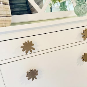 May include: White dresser with four drawers and brown flower-shaped drawer pulls. The top drawer is open.