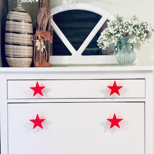 May include: White dresser with four red star-shaped drawer pulls. The dresser has two drawers and a cabinet door.