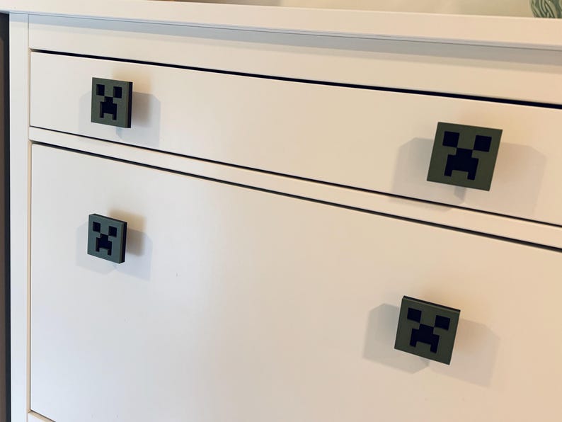 May include: White dresser with four drawers. Each drawer has a black and green Minecraft Creeper face pull.