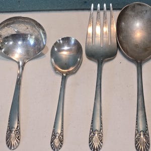 May include: A set of vintage silverware, including a ladle, a spoon, a fork, and a smaller spoon. The silverware is made of a shiny, silver-colored metal. The handles have a decorative floral design.