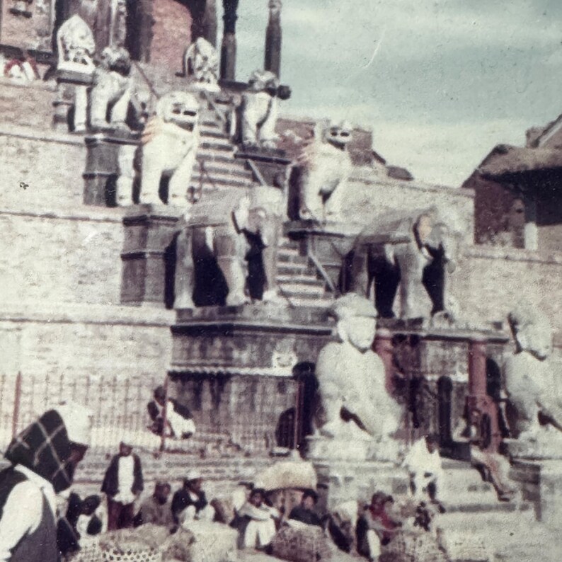 May include: A stone temple with a staircase leading up to the entrance. There are several statues of elephants and lions on the steps. People are gathered at the bottom of the stairs.