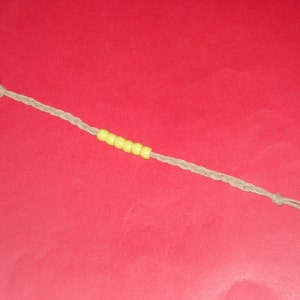 May include: A keychain with a silver ring and a braided beige cord. The cord is adorned with six yellow beads. The end of the cord is knotted and has several loose strands.