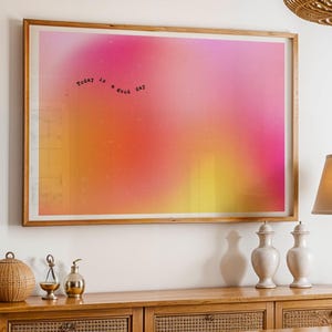 May include: A framed art print with a pink, orange, and yellow gradient. The text "today is a good day" is written on the print. The artwork hangs above a wooden cabinet with decorative items, including a lamp and vases.