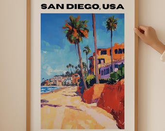 May include: A framed print of a colorful painting depicting a beach scene in San Diego, USA. The painting features palm trees, buildings, and a sandy beach with blue water in the background. The text "SAN DIEGO, USA" is printed in black at the top of the print.