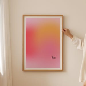 Könnte beinhalten: Ein gerahmter Kunstdruck mit einem Farbverlauf aus Rosa, Orange und Gelb. Die Worte "my happy place" sind in kleiner, schwarzer Schrift unten rechts gedruckt. Der Rahmen ist hellbraun.