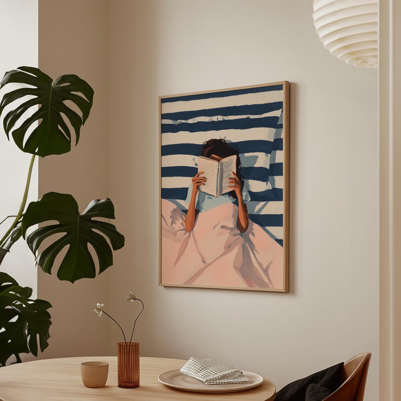 a cozy indoor setting with a framed painting of a person reading a book, a table with a vase of flowers, and a potted plant.