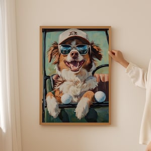 May include: A framed print featuring a dog wearing sunglasses and a golf cap, driving a golf cart. The dog has brown and white fur and is smiling. Two golf balls are in front of the dog. The background is green.