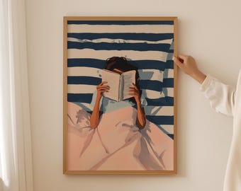May include: A framed art print depicts a person reading in bed. The artwork features a person with dark hair, reading a book under a blue and white striped comforter. The bed linens are a soft pink. The frame is a light wood color.
