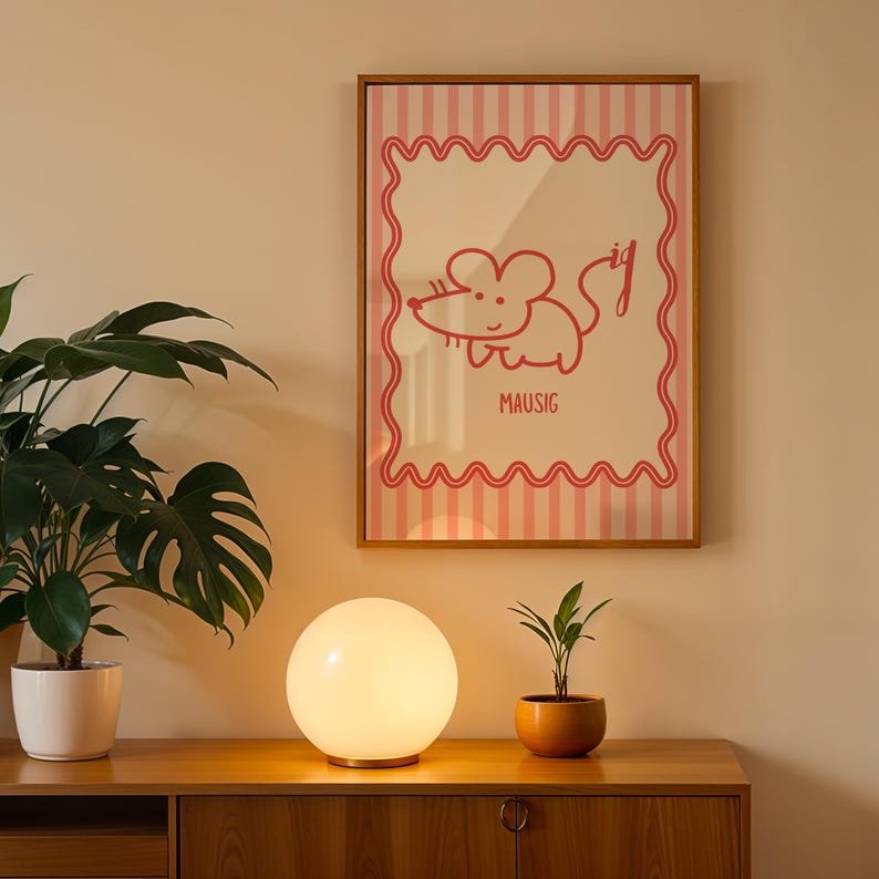 May include: A framed poster with a pink and white striped design and a red cartoon mouse illustration. The word "MAUSIG" is below the illustration. A white globe lamp and potted plants sit on a wooden cabinet.