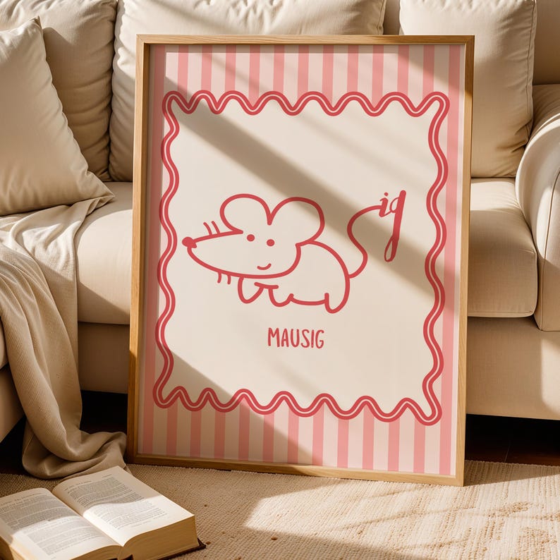 May include: A framed print with a cartoon mouse illustration in red. The mouse is drawn with simple lines and has a smiling expression. The word "MAUSIG" is printed below the mouse in red. The background has pink stripes.