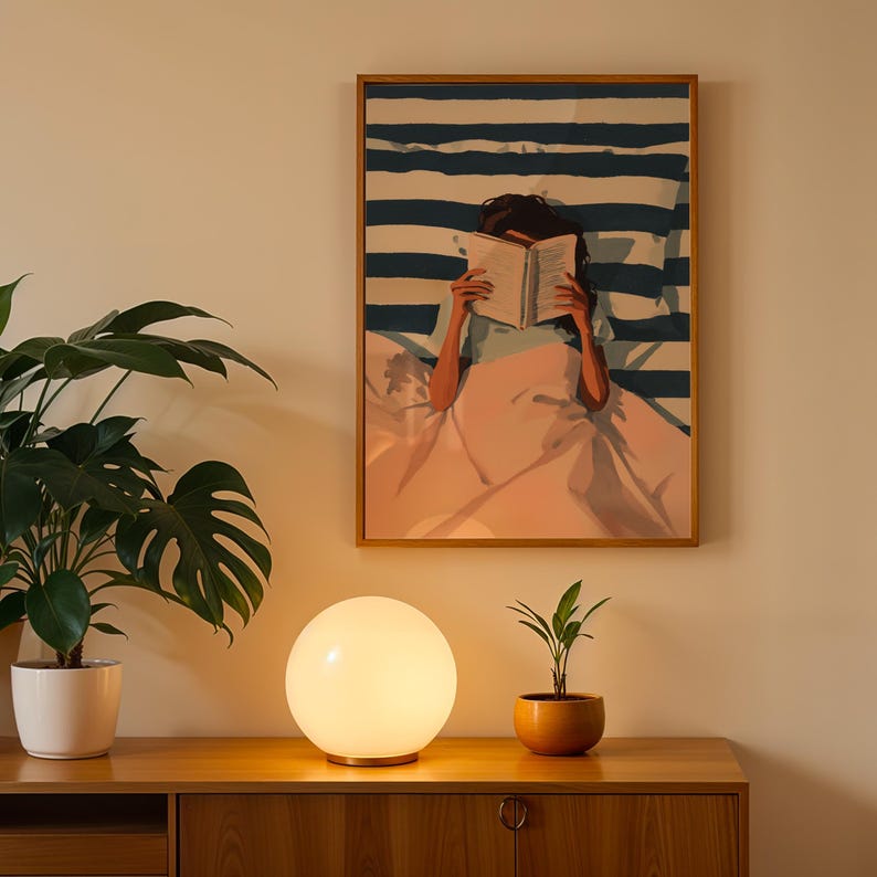 a wooden cabinet with a lamp on top, a potted plant, and a framed painting of a woman reading a book.