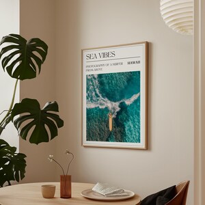 May include: A framed print with the text "SEA VIBES" and "PHOTOGRAPHY OF A SURFER FROM ABOVE" in black text. The image shows a surfer on a surfboard in the ocean, photographed from above. The text "HAWAII" is in the top right corner.