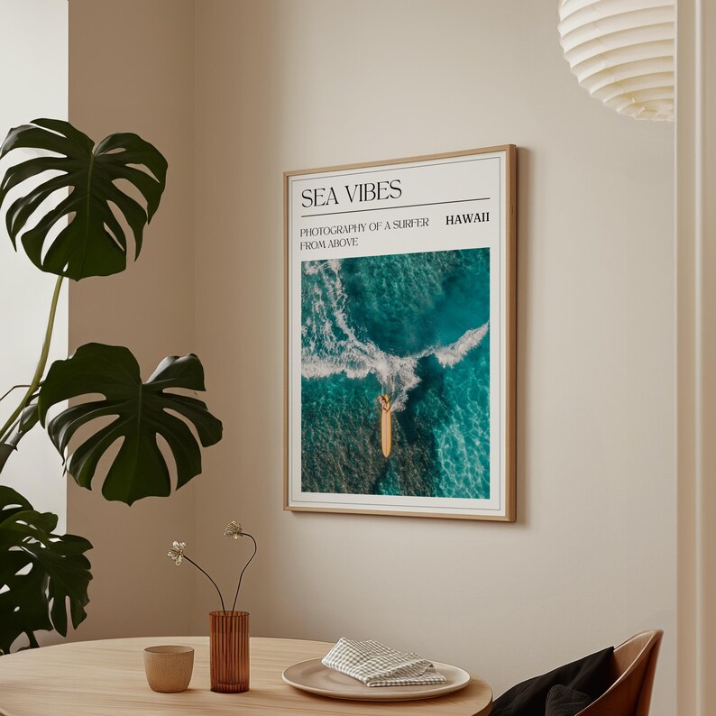 May include: A framed print with the text "SEA VIBES" and "PHOTOGRAPHY OF A SURFER FROM ABOVE" in black text. The image shows a surfer on a surfboard in the ocean, photographed from above. The text "HAWAII" is in the top right corner.