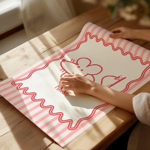 May include: A rolled-up mat with a pink and white striped border and a wavy pink outline. The mat features a cartoon mouse illustration and the word "MUSIC" in pink. The mat is on a wooden surface.
